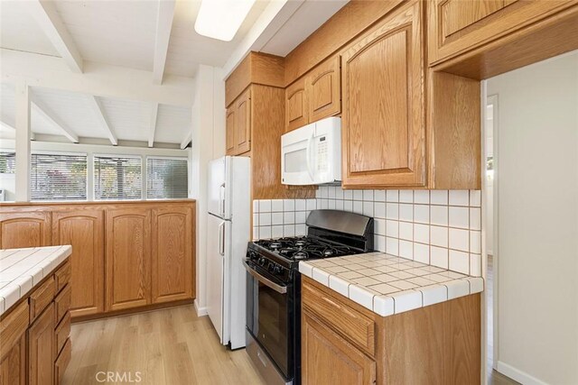 kitchen featuring decorative backsplash, beam ceiling, light hardwood / wood-style flooring, tile counters, and white appliances