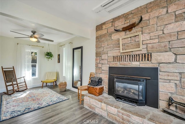 sitting room with ceiling fan, a stone fireplace, and wood-type flooring