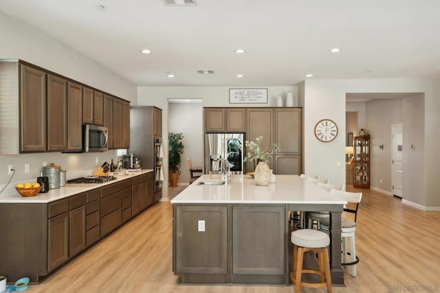 kitchen with a large island with sink, a kitchen breakfast bar, stainless steel appliances, sink, and light hardwood / wood-style floors