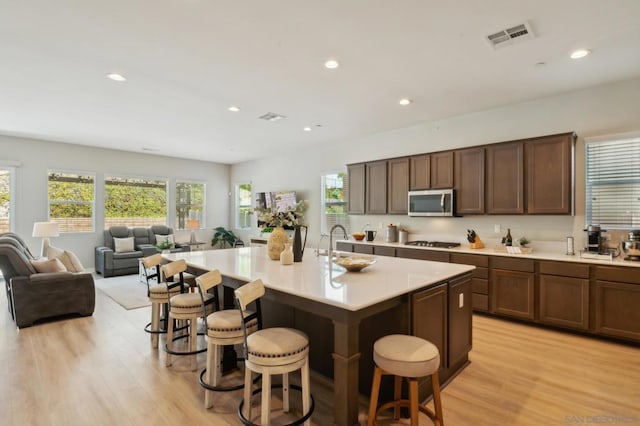 kitchen with a breakfast bar area, appliances with stainless steel finishes, light wood-type flooring, and an island with sink