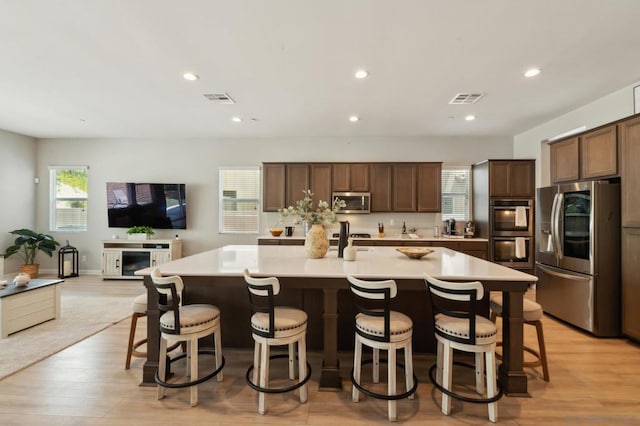 kitchen with a spacious island, light hardwood / wood-style floors, stainless steel appliances, and a kitchen breakfast bar