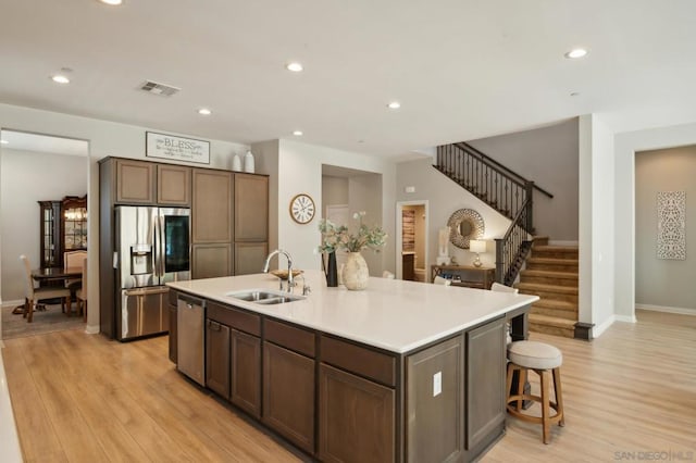 kitchen featuring sink, appliances with stainless steel finishes, a kitchen island with sink, and light wood-type flooring