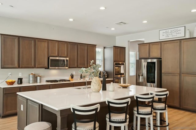 kitchen featuring a kitchen island with sink, stainless steel appliances, sink, a kitchen bar, and light wood-type flooring