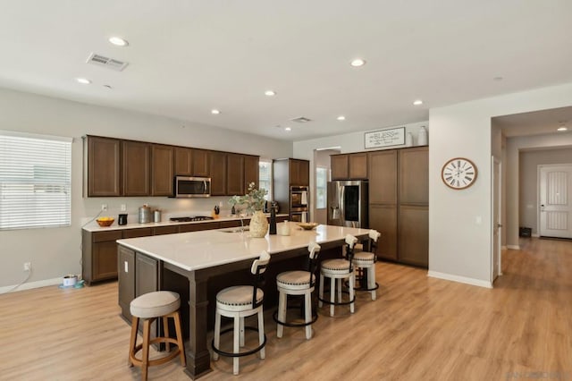 kitchen with stainless steel appliances, light wood-type flooring, a center island with sink, and a kitchen breakfast bar