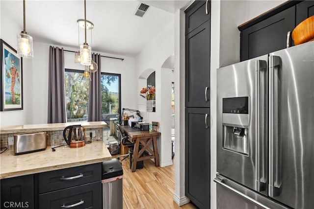 kitchen with light stone countertops, stainless steel fridge, light hardwood / wood-style flooring, and pendant lighting