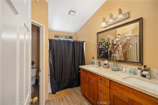 bathroom with vanity, toilet, wood-type flooring, and vaulted ceiling