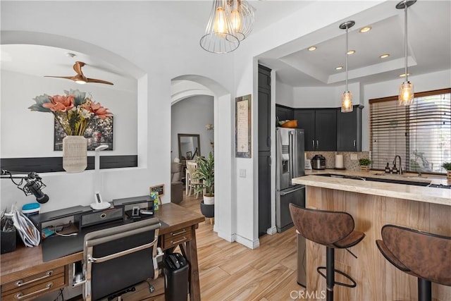 kitchen featuring sink, tasteful backsplash, light stone counters, stainless steel refrigerator with ice dispenser, and light hardwood / wood-style floors