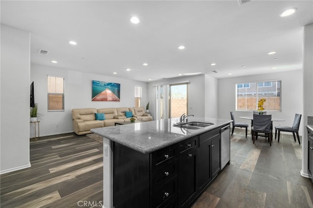 kitchen featuring dishwasher, sink, dark hardwood / wood-style floors, light stone countertops, and an island with sink