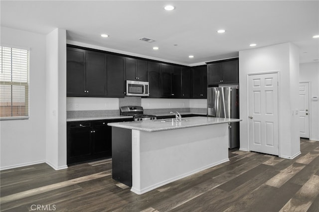 kitchen featuring sink, stainless steel appliances, light stone counters, dark hardwood / wood-style floors, and a center island with sink