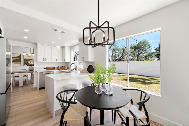 kitchen featuring kitchen peninsula, stainless steel appliances, light wood-type flooring, white cabinetry, and sink