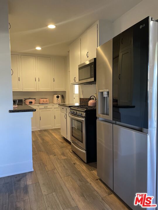 kitchen with white cabinetry, stainless steel appliances, and wood-type flooring