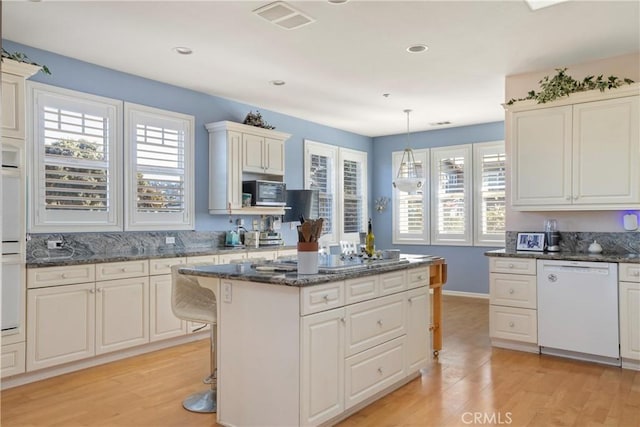 kitchen with pendant lighting, white dishwasher, a kitchen island, dark stone countertops, and light hardwood / wood-style floors