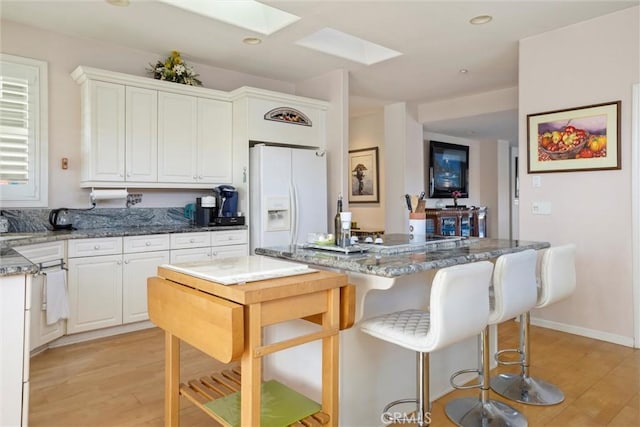 kitchen featuring light hardwood / wood-style floors, white fridge with ice dispenser, dark stone counters, and a skylight