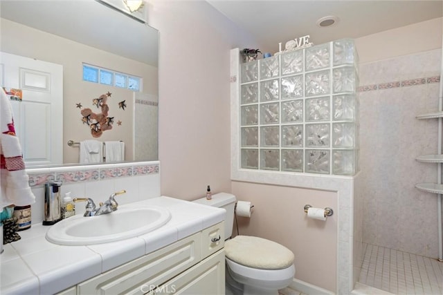 bathroom with tiled shower, vanity, and toilet