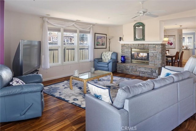 living room with a stone fireplace, ceiling fan, and dark wood-type flooring