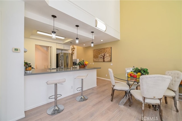 kitchen featuring a kitchen breakfast bar, kitchen peninsula, stainless steel fridge, decorative light fixtures, and a raised ceiling