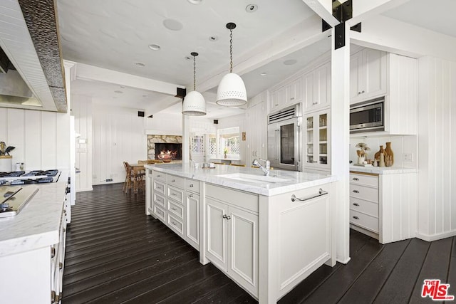 kitchen featuring a spacious island, sink, pendant lighting, built in appliances, and white cabinetry