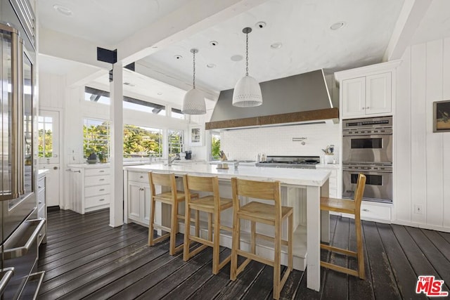 kitchen featuring appliances with stainless steel finishes, dark hardwood / wood-style flooring, a breakfast bar, white cabinets, and range hood