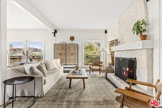 living room featuring beamed ceiling and a stone fireplace