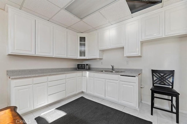 kitchen with light tile patterned flooring, sink, white cabinets, and a drop ceiling