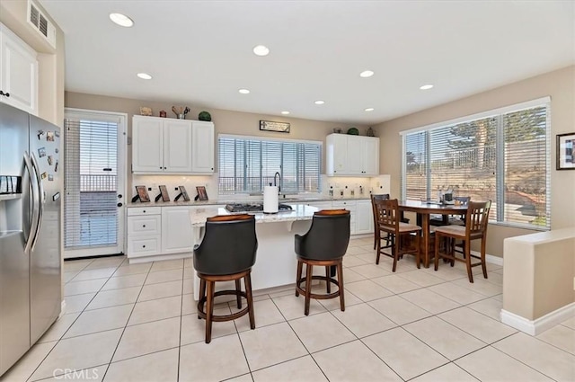 kitchen featuring stainless steel fridge, white cabinetry, a kitchen island, and a kitchen breakfast bar