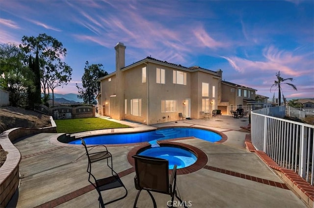 pool at dusk with an in ground hot tub, a patio, an outdoor fireplace, and a lawn