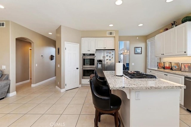 kitchen with white cabinets, light stone counters, a kitchen island, and stainless steel appliances