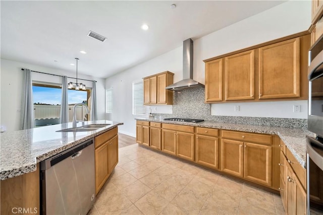 kitchen featuring appliances with stainless steel finishes, light stone counters, sink, wall chimney range hood, and hanging light fixtures