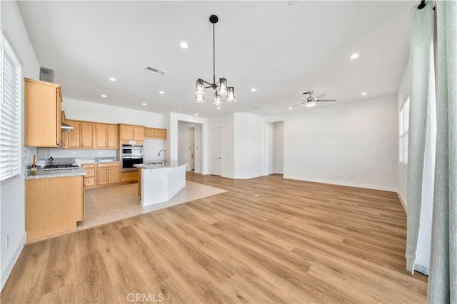 kitchen with a kitchen island with sink, sink, hanging light fixtures, and light wood-type flooring