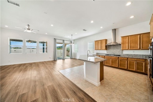 kitchen featuring wall chimney exhaust hood, sink, plenty of natural light, and a kitchen island with sink