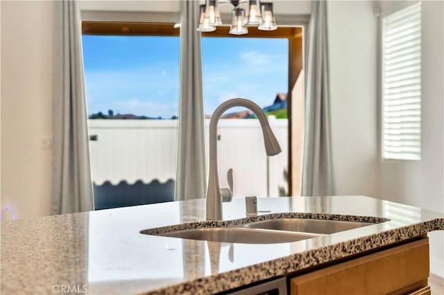 interior details with light stone countertops, pendant lighting, a notable chandelier, and sink