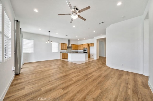 unfurnished living room featuring ceiling fan with notable chandelier and light hardwood / wood-style floors