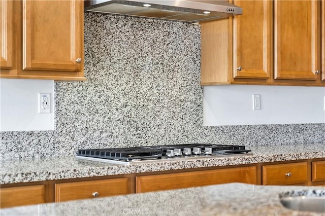 kitchen with stainless steel gas stovetop, wall chimney exhaust hood, light stone countertops, and tasteful backsplash