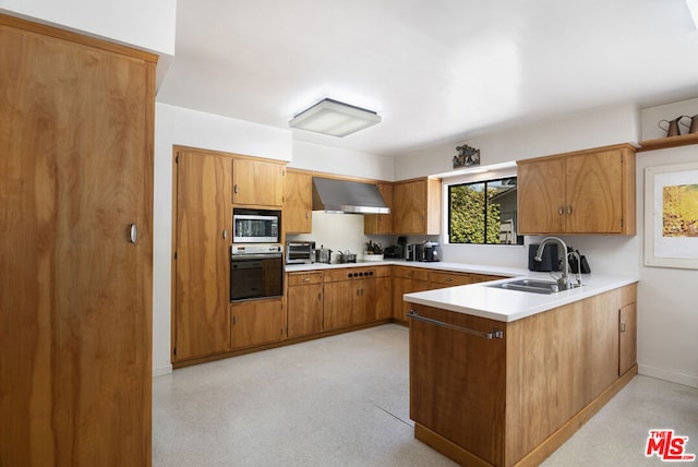 kitchen featuring kitchen peninsula, wall chimney range hood, sink, black oven, and stainless steel microwave