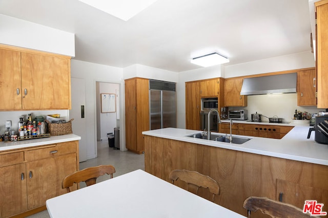 kitchen featuring built in appliances, wall chimney exhaust hood, kitchen peninsula, and sink