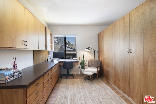 home office with built in desk and light hardwood / wood-style floors