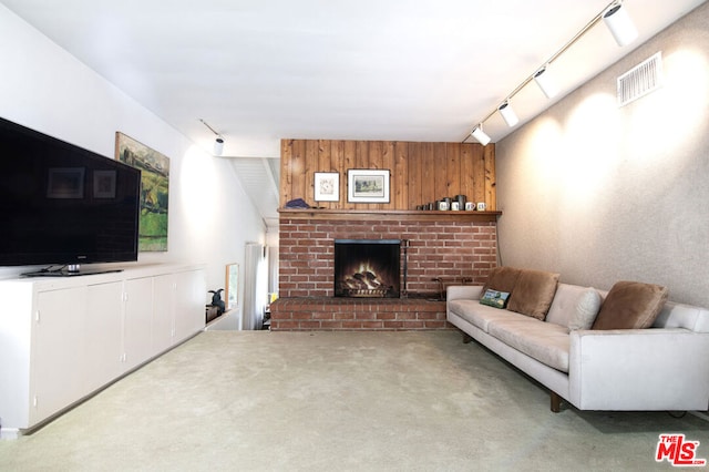 living room with a brick fireplace, light carpet, wooden walls, and track lighting