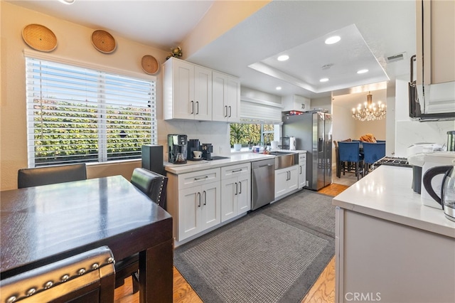 kitchen with stainless steel appliances, tasteful backsplash, a tray ceiling, white cabinets, and light wood-type flooring