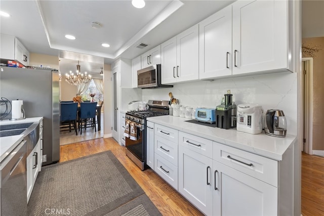 kitchen featuring light hardwood / wood-style flooring, white cabinets, stainless steel appliances, and an inviting chandelier