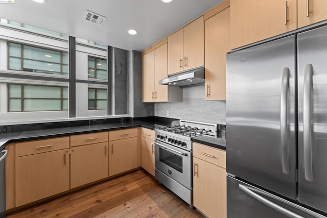 kitchen featuring backsplash, light brown cabinetry, stainless steel appliances, and hardwood / wood-style flooring