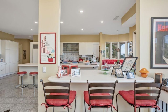 kitchen featuring kitchen peninsula, backsplash, white cabinetry, and a breakfast bar area