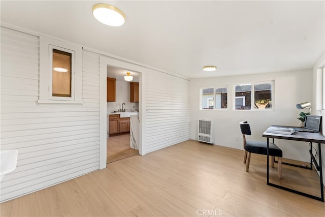 office space with light wood-type flooring, heating unit, and sink