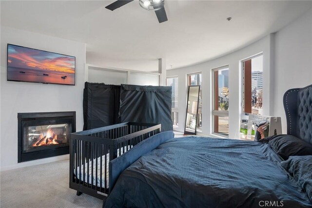 bedroom featuring a multi sided fireplace, ceiling fan, and carpet