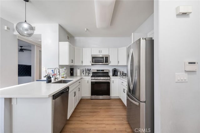 kitchen with sink, kitchen peninsula, light hardwood / wood-style floors, decorative light fixtures, and appliances with stainless steel finishes