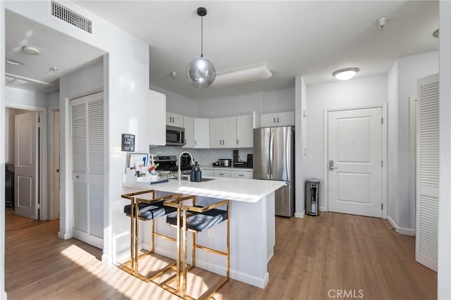 kitchen with sink, kitchen peninsula, appliances with stainless steel finishes, white cabinets, and light wood-type flooring