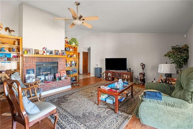 living room featuring hardwood / wood-style floors, vaulted ceiling, a brick fireplace, and ceiling fan