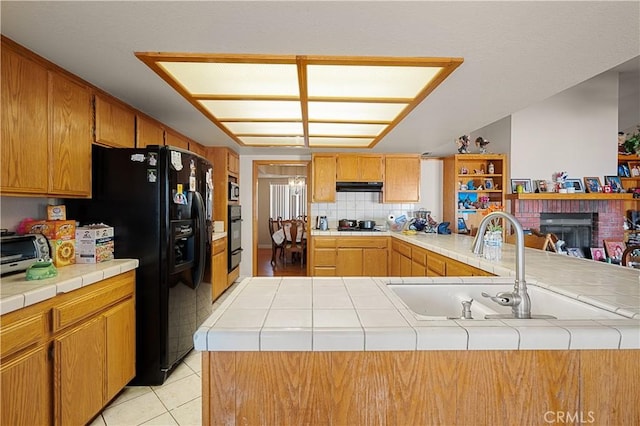 kitchen featuring light tile patterned floors, a brick fireplace, tile counters, and black appliances