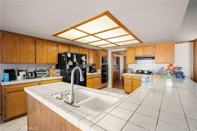 kitchen featuring tile counters, an island with sink, black appliances, and sink