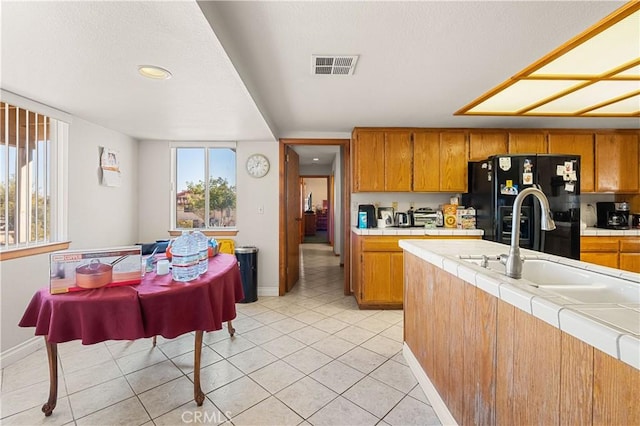 kitchen featuring tile countertops, black fridge with ice dispenser, light tile patterned flooring, and sink