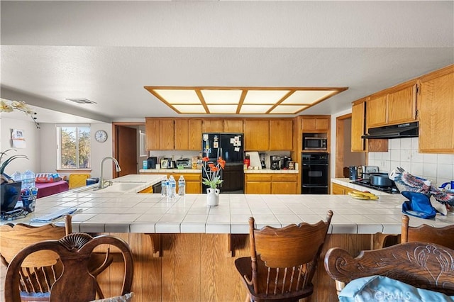 kitchen featuring kitchen peninsula, ventilation hood, tile counters, and black appliances